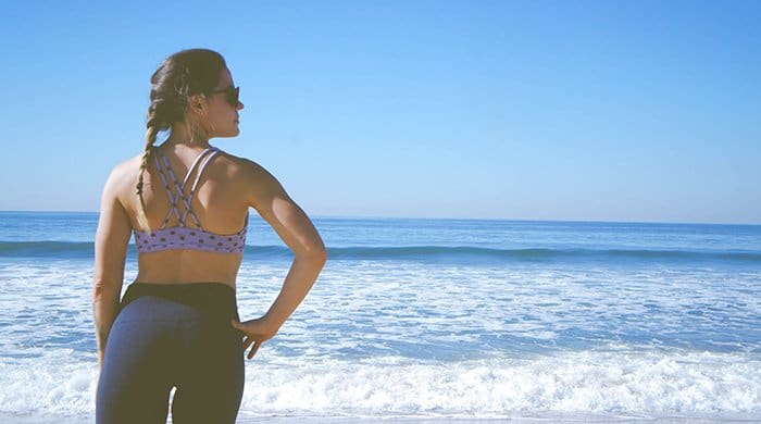 A woman in her workout gear sanding on the beach because it is one of her rest days