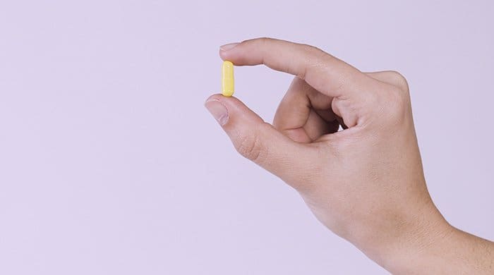 a woman holding a skin probiotic pill between her fingers