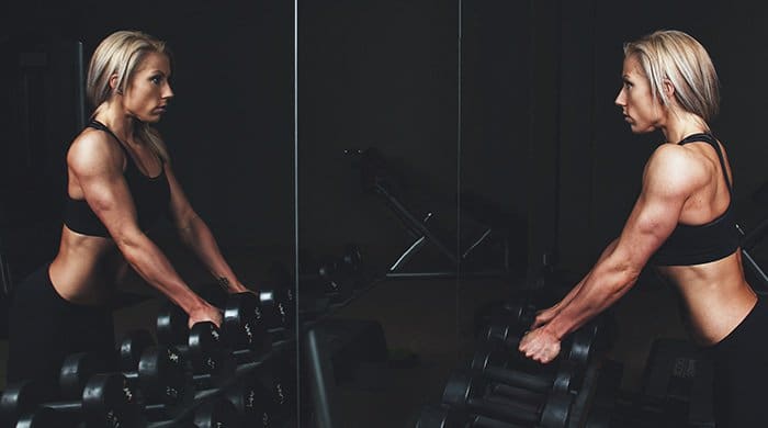 A female bodybuilder standing in front of a mirror with weights to symbolise the viral post about a real-life bodybuilder's transformation photos