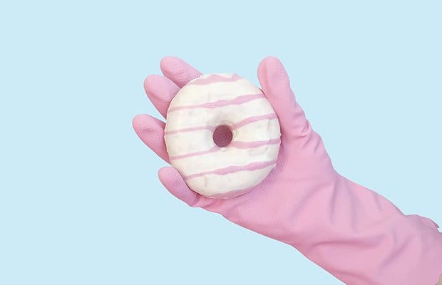 Person wearing a pink glove holding a white donut to illustrate a point about anal bleaching