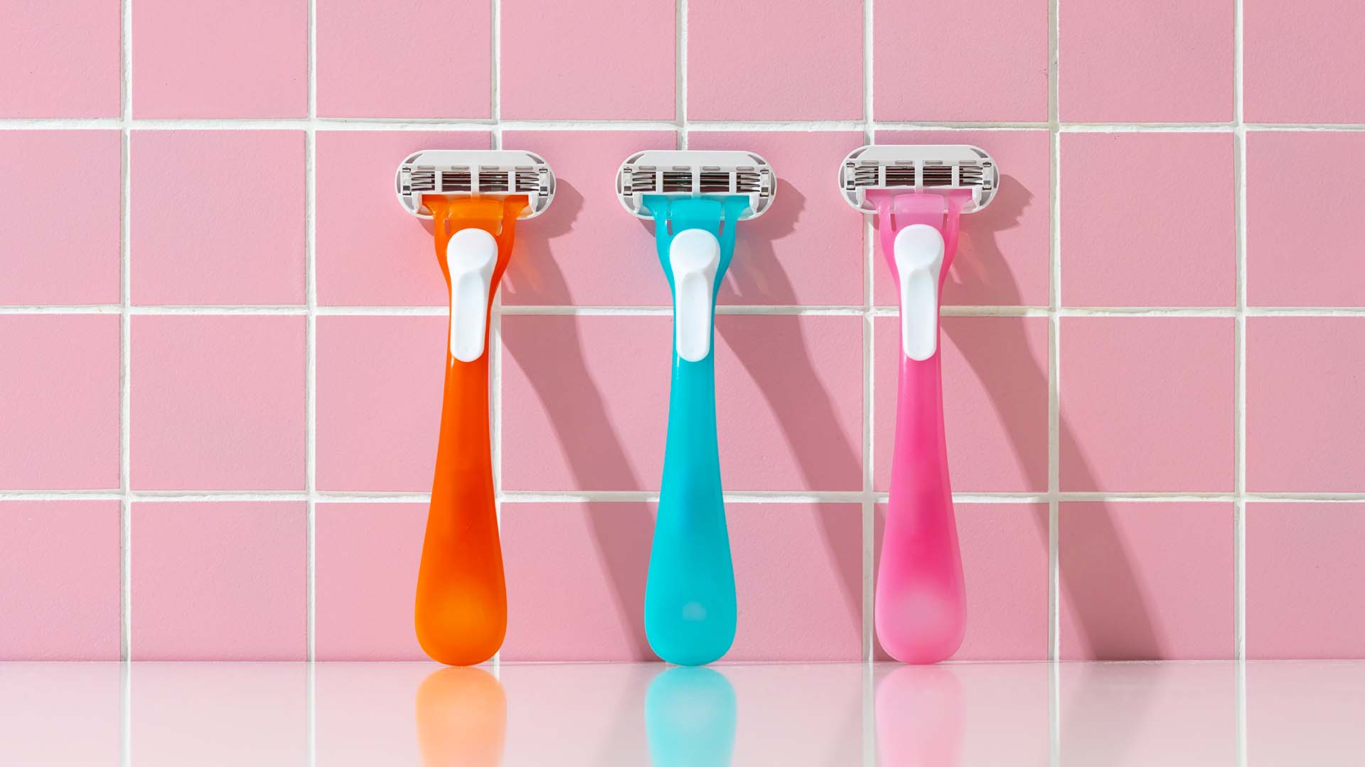 Three razors on pink bathroom background