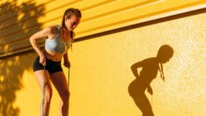 Female athlete stretching resistance band while exercising by yellow wall