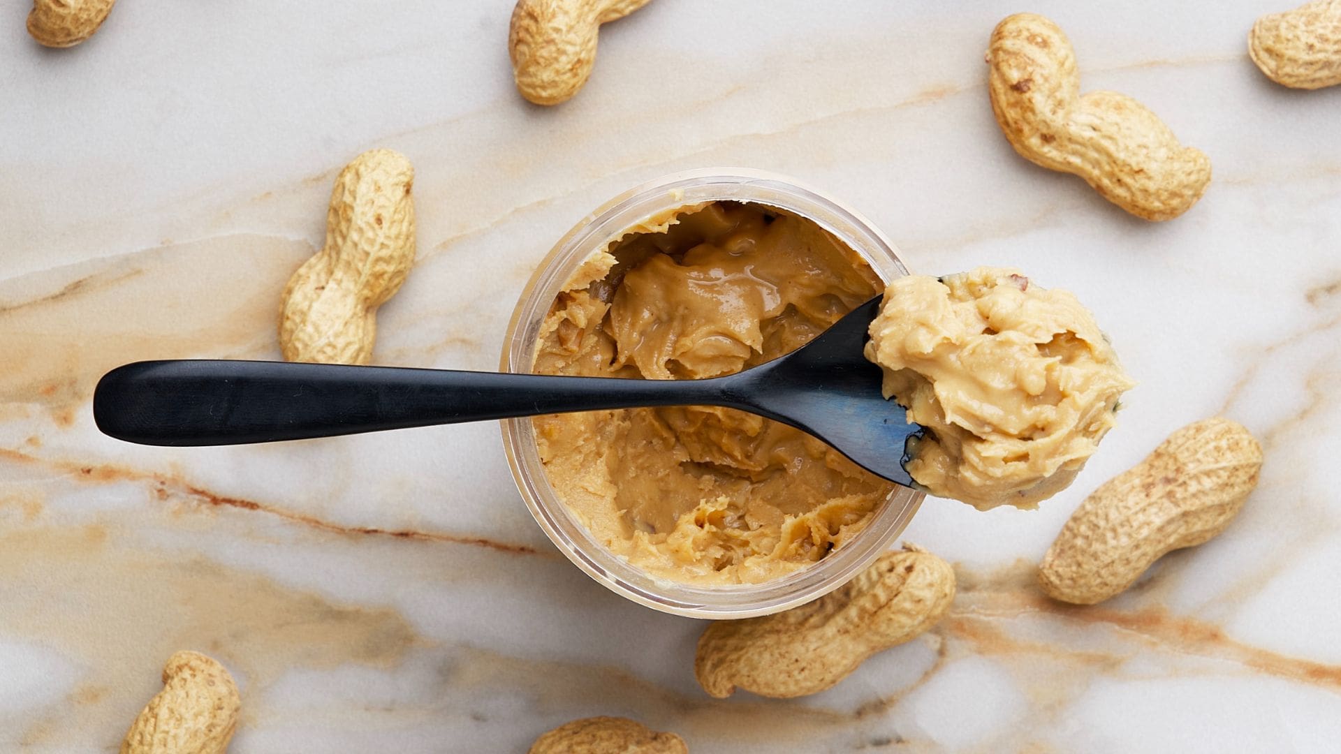 picture of nut butter made from nut butter recipe with shelled peanuts around it and a spoon on top