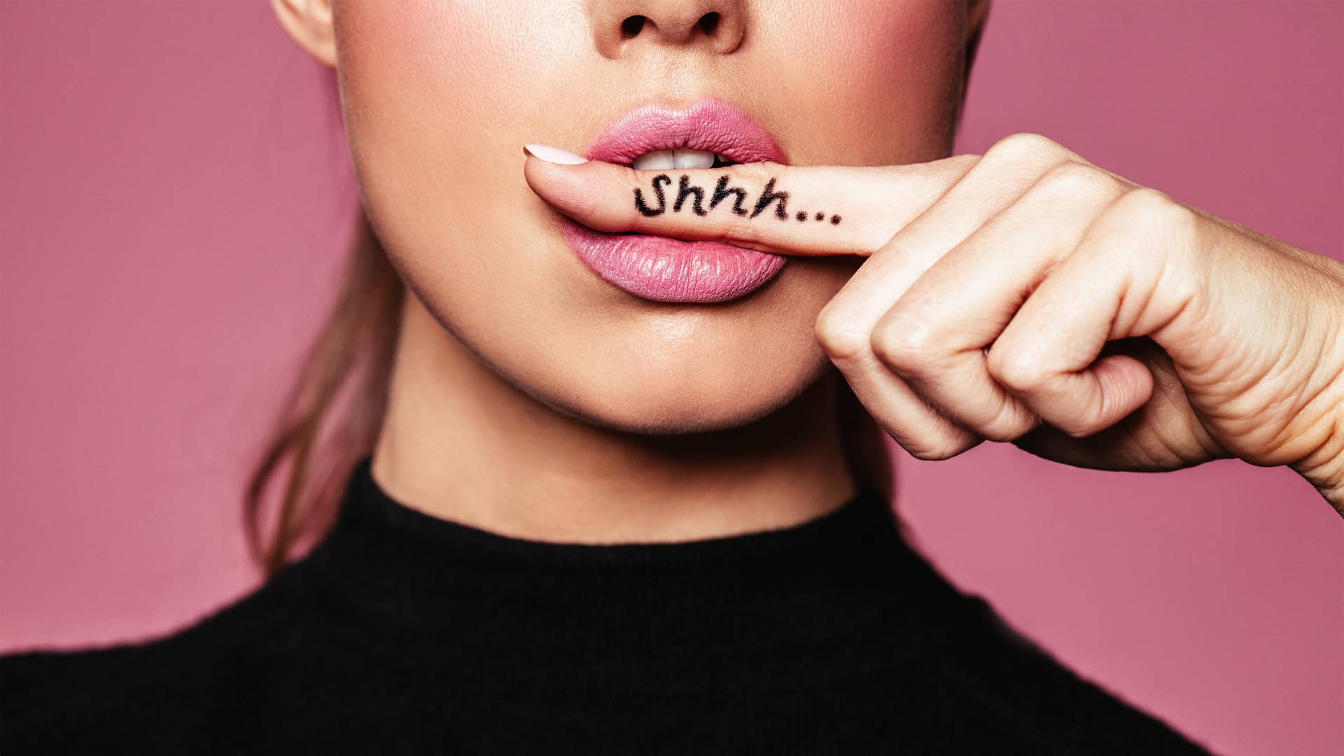 Shh! Women's secrets. Cropped shot of female with finger in mouth. Closeup portrait of young woman is showing a sign of silence with shhh written on the finger for quiet vibrators.