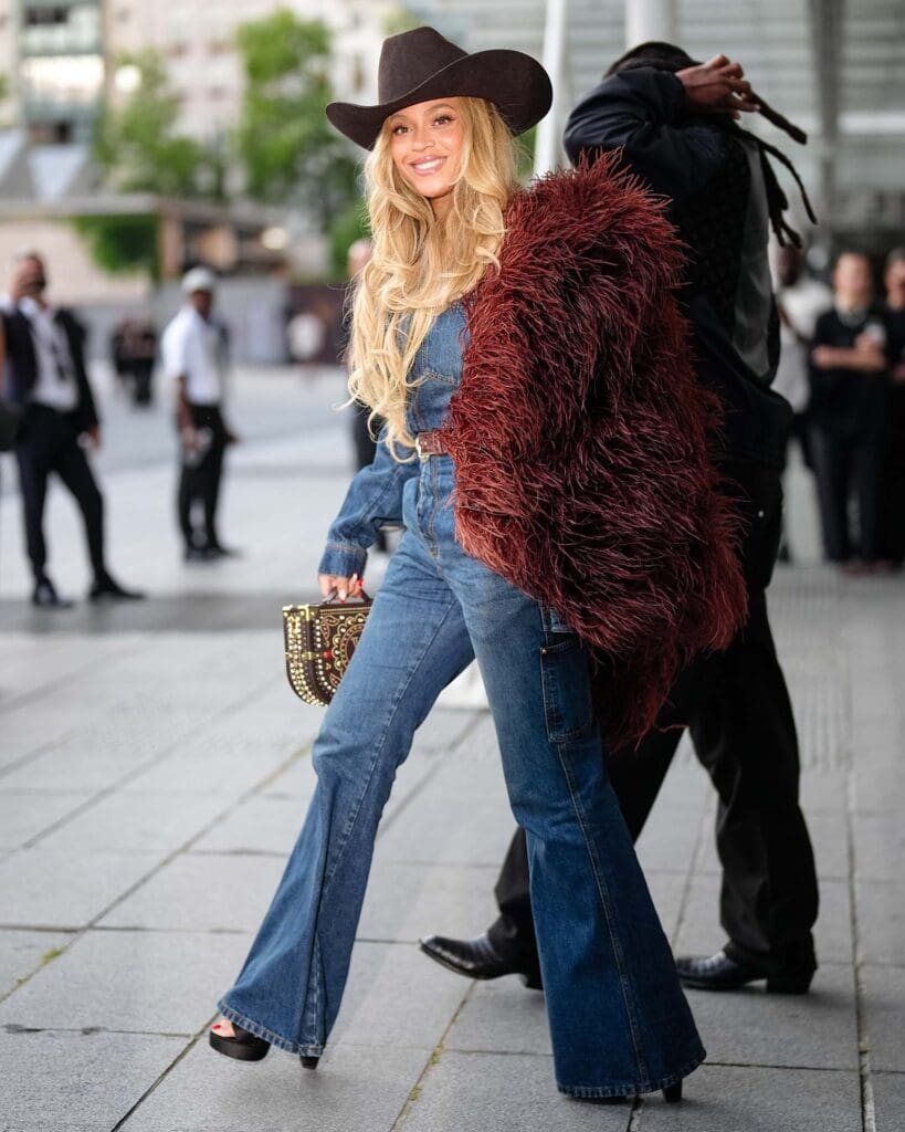PARIS, FRANCE - JUNE 24: Beyoncé Knowles / Beyonce wears a cowboy hat, a burgundy faux fur fluff coat on one shoulder, a blue denim jacket, blue flared denim pants / jeans, during the Louis Vuitton Menswear Spring/Summer 2026 show as part of Paris Fashion Week on June 24, 2025 in Paris, France.