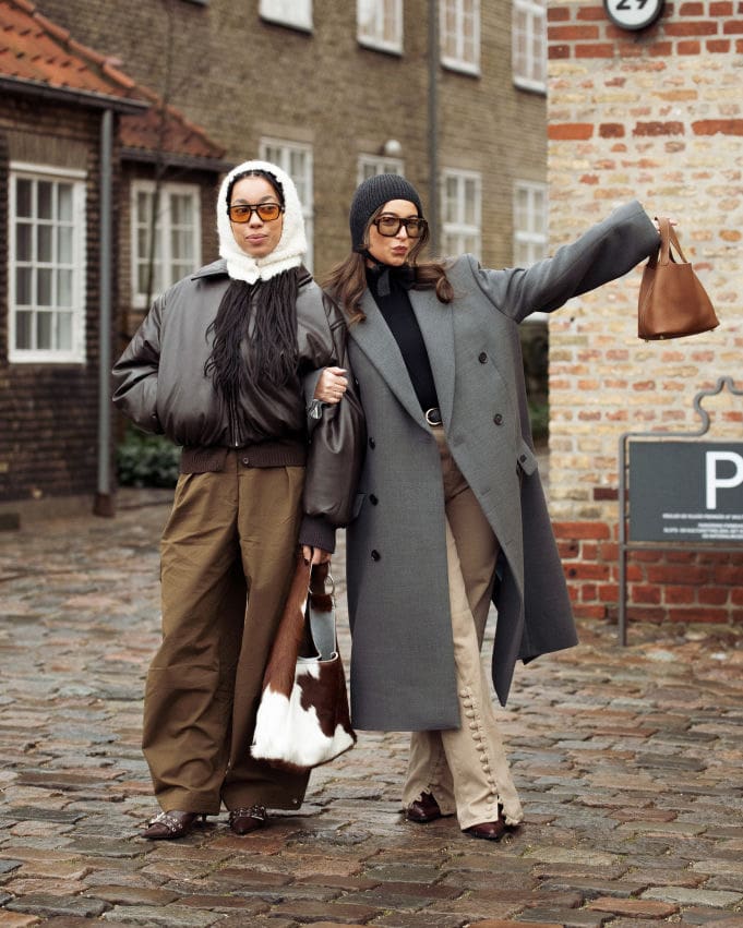 COPENHAGEN, DENMARK - JANUARY 27: Amaka Hamelijnck wears wide brown pants, dark brown leather jacket, white hat and cow print bag and Benthe Liem wears beige pants, black turtle neck, grey coat and dark grey knitted hat outside the OpéraSport show during the Copenhagen Fashion Week Autumn/Winter 2025 on January 27, 2025 in Copenhagen, Denmark.
