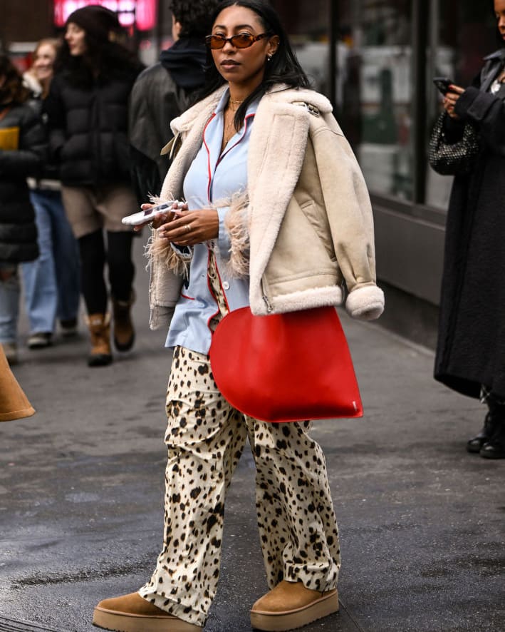 NEW YORK, NEW YORK - FEBRUARY 09: A guest is seen wearing a cream coat, blue shirt, cow print pants and tan boots with red bag outside the Lapointe show during NYFW F/W 2025 on February 09, 2025 in New York City.