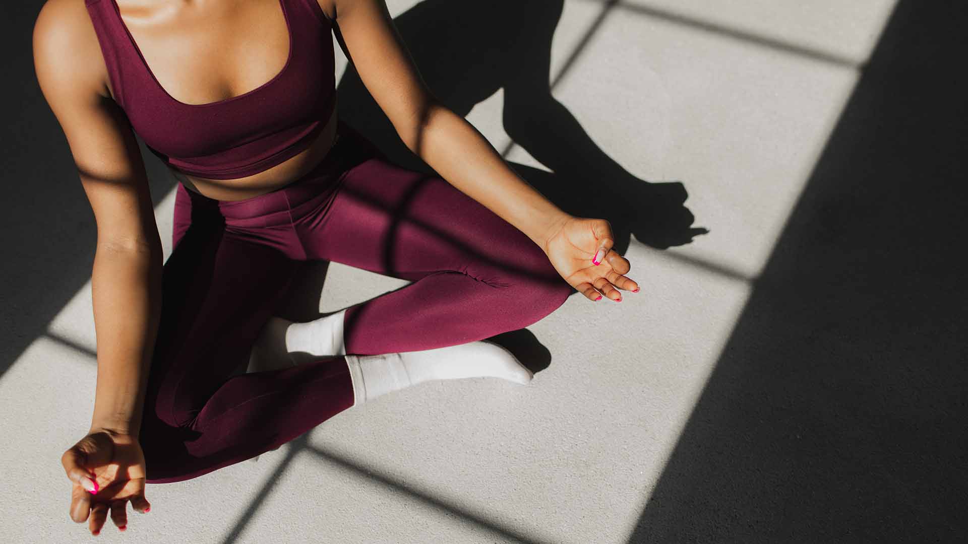 Fit woman with braided hair practicing yoga and doing Padmasana pose on white background.