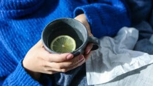 Woman holding a cup of lemon water with a cold/flu